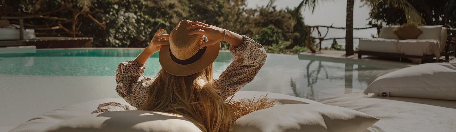 woman sitting by pool holding her straw hat