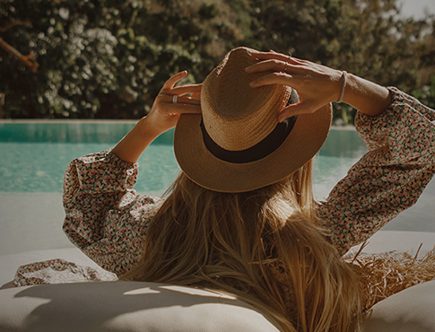 woman setting by the pool holding her straw hat